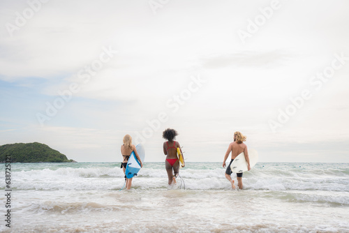 Two women and young man holding surfboards ready to walk into the sea to surf.