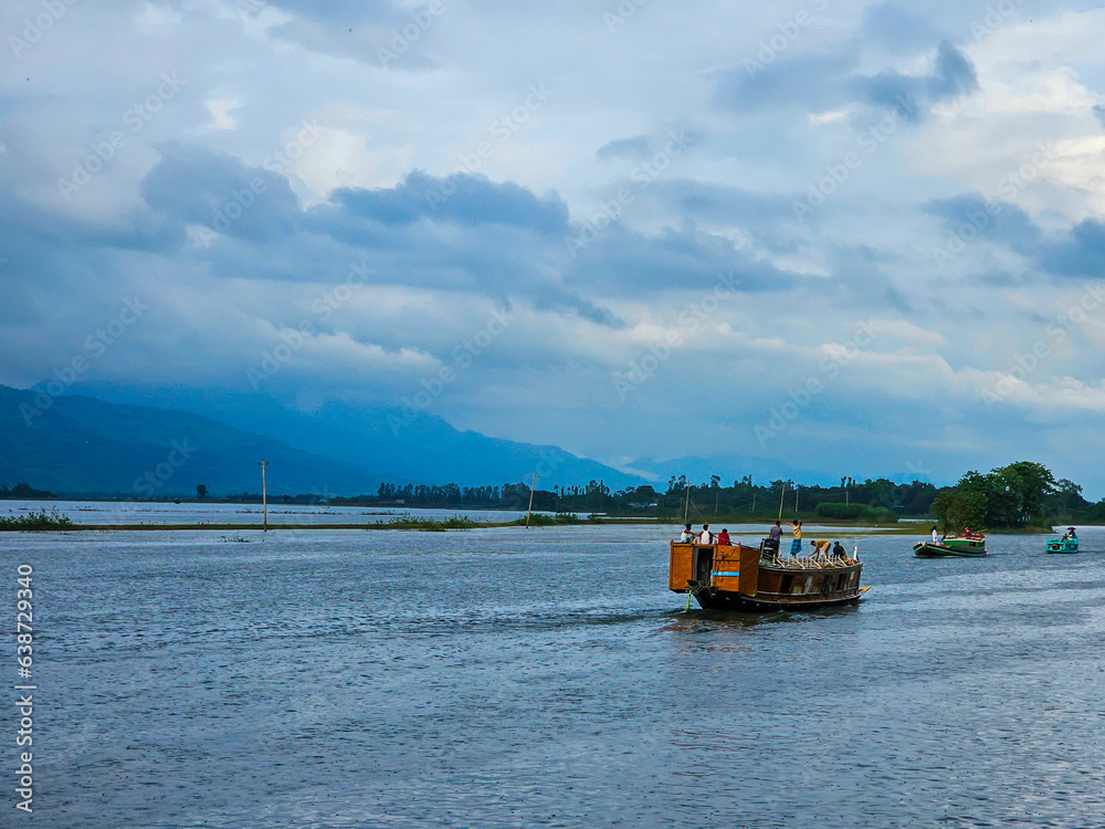 Tanguar Haor Houseboat sailing on the river near the India border in Bangladesh during the rainy season with the beautiful Meghalayan hills at the background.
