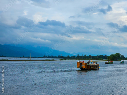 Tanguar Haor Houseboat sailing on the river near the India border in Bangladesh during the rainy season with the beautiful Meghalayan hills at the background. © Asif