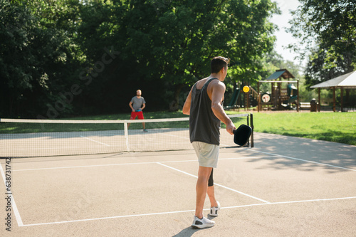 Two young adults playing a game of pickleball near a playground © Cavan