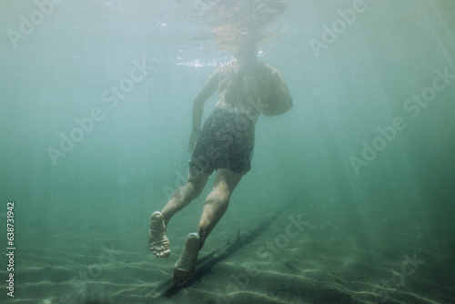 A young male floats freely underwater in a lake.