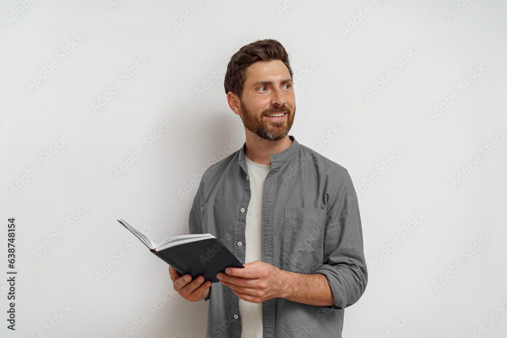 Smiling man in casual clothes standing with open notepad and looking at side white background Smiling man in casual clothes standing with open notepad and looking at side white background