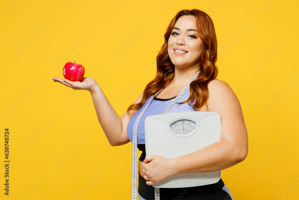 Side view young chubby overweight plus size big fat fit woman wear blue top measure tape warm up training hold scales apple isolated on plain yellow background studio home gym. Workout sport concept. Side view young chubby overweight plus size big fat fit woman wear blue top measure tape warm up training hold scales apple isolated on plain yellow background studio home gym. Workout sport concept.