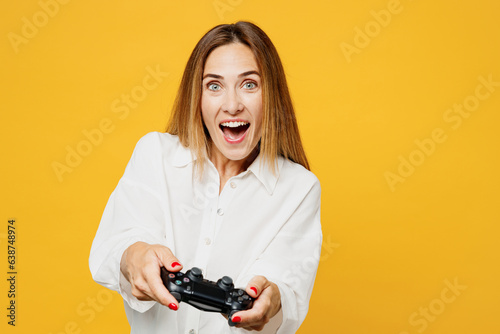 Young excited gambling caucasian happy woman she wears white shirt casual clothes hold in hand play pc game with joystick console isolated on plain yellow background studio portrait Lifestyle concept