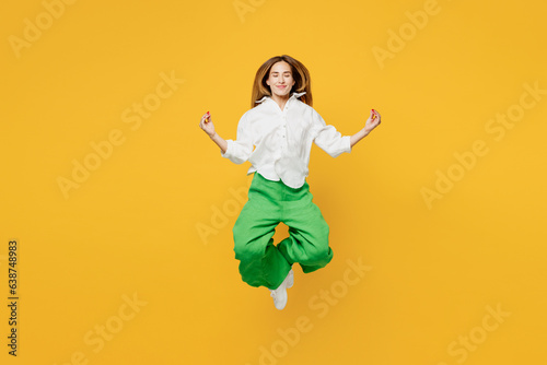 Full body young spiritual happy woman she wearing white shirt casual clothes jump high hold spreading hands in yoga om aum gesture relax meditate try to calm down isolated on plain yellow background.