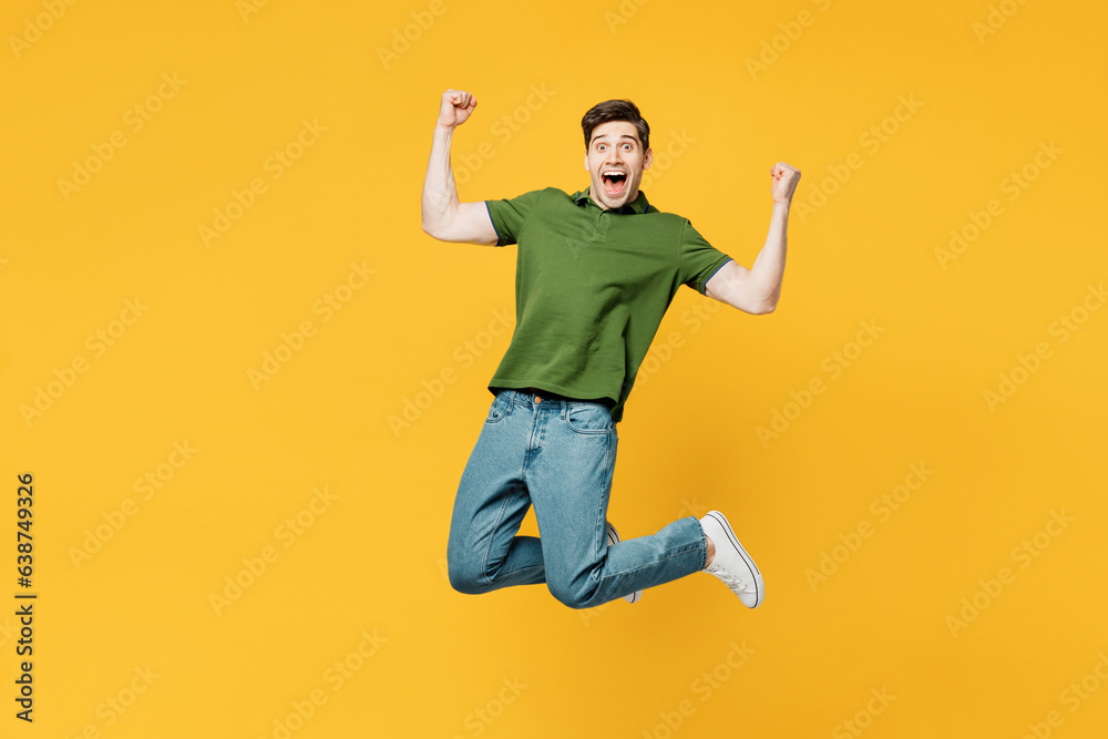 Full body young overjoyed excited cool happy man he wears green t-shirt casual clothes jump high do winner gesture clench fist isolated on plain yellow background studio portrait. Lifestyle concept. Full body young overjoyed excited cool happy man he wears green t-shirt casual clothes jump high do winner gesture clench fist isolated on plain yellow background studio portrait. Lifestyle concept.