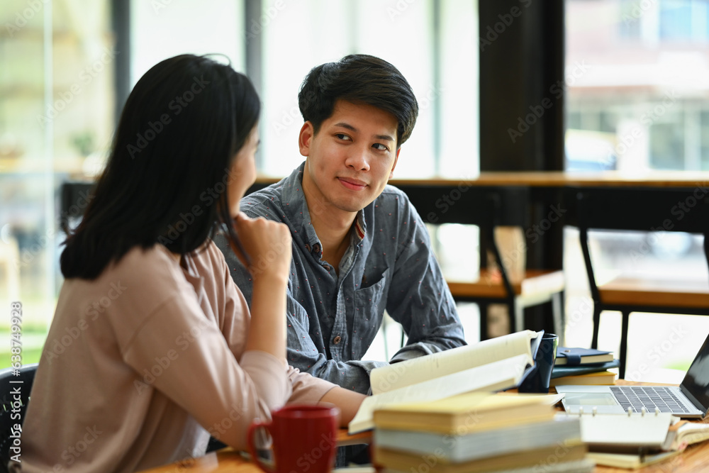 Asian male and classmate sitting at table preparing for exams finding information for their college assignment Asian male and classmate sitting at table preparing for exams finding information for their college assignment