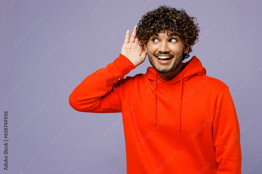 Young curious nosy Indian man wear red orange hoody casual clothes try to hear you overhear listening intently isolated on plain pastel light purple color backgroundstudio portrait. Lifestyle concept.