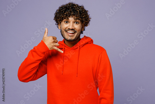 Young smiling happy Indian man wear red orange hoody casual clothes doing phone gesture like says call me back isolated on plain pastel light purple color background studio portrait Lifestyle concept