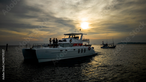 Silhouettes of people enjoying drinks on a catamaran at sunset