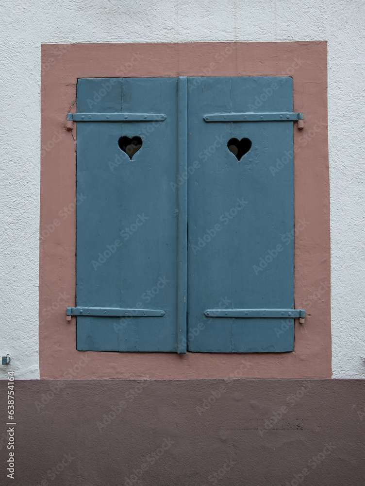 Window with blue closed wooden shutters on white stone wall background.
