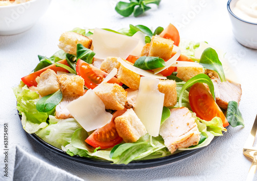 Classic Caesar salad with chicken, iceberg salad, croutons, parmesan cheese and caesar dressing. Black table background, top view