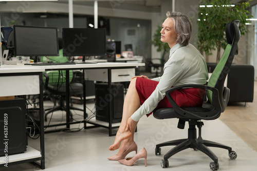 Caucasian woman massaging her tired legs while sitting in the office. 