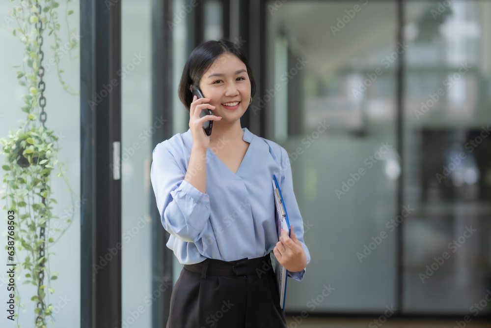 Happy Asian businesswoman talking on mobile phone and holding clipboard in modern office. Happy Asian businesswoman talking on mobile phone and holding clipboard in modern office.