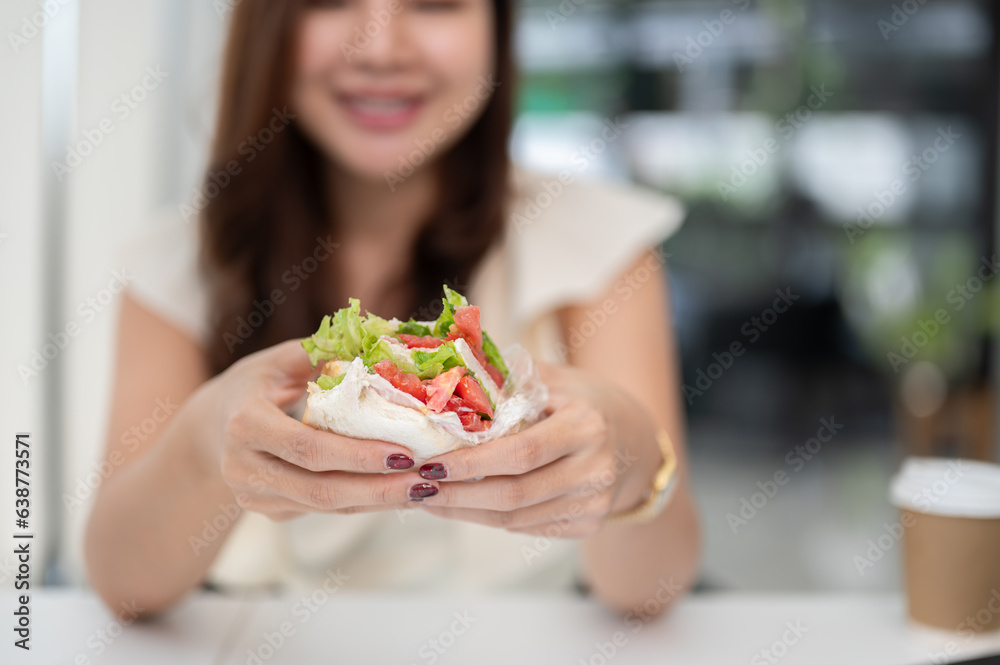 Close-up image of a businesswoman holding a sandwich, eating a sandwich at her desk Close-up image of a businesswoman holding a sandwich, eating a sandwich at her desk