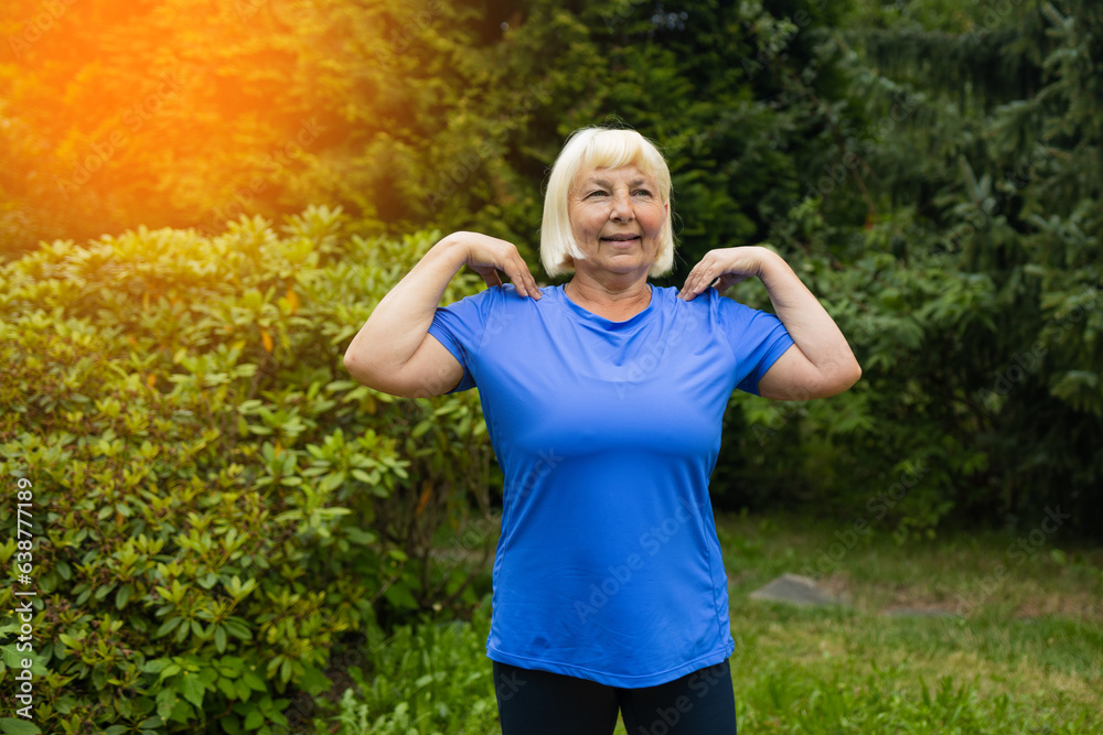 Happy caucasian 50s elderly woman stretching hands before exercise at park outdoor. Old female training at summer sunny day. High quality photo