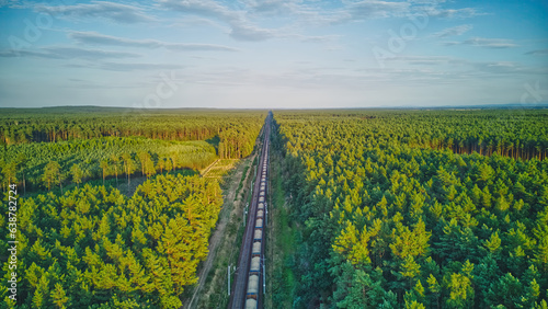 Electric locomotive with railway wagons rides on railroad. Transportation, delivery export and import between cities and countries. Aerial view over train riding through forest.