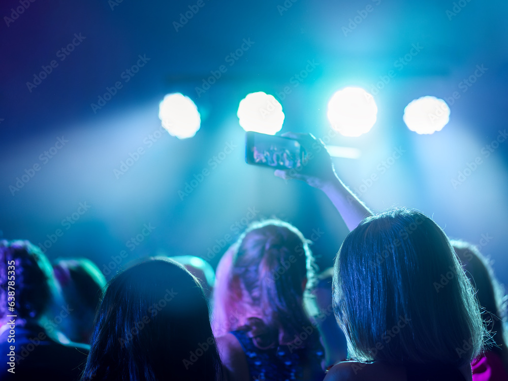 Young woman recording a concert with her cell phone. Nightlife and disco concept. Selective Focus