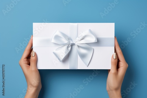 Woman holding white present box with vivid silver ribbon bow as presenf for Christmas, fathers day, birthday on light blue background. Flat lay, copy space