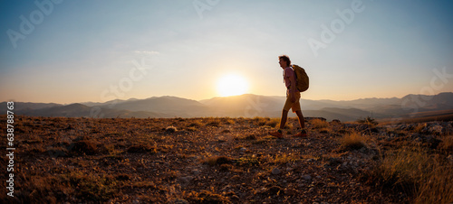 man with a backpack walks along the path against the backdrop of mountains. hiking in the mountains with a backpack.
