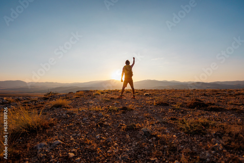 An active young man feels free. A confident man stands on a mountain against the background of a sunset. Experience freedom in the heart of nature.