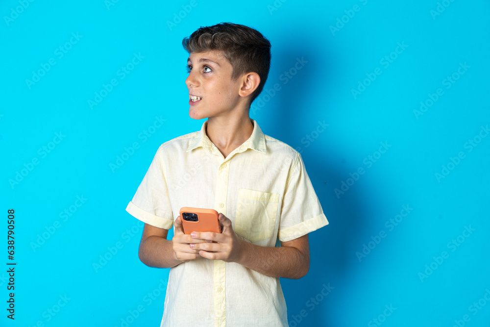 Beautiful kid boy wearing casual shirt holding a smartphone and looking sideways at blank copyspace. Beautiful kid boy wearing casual shirt holding a smartphone and looking sideways at blank copyspace.