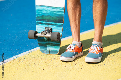 Close-up of male legs in sneakers standing with skateboard on a yellow and blue concrete platform, summer vibe