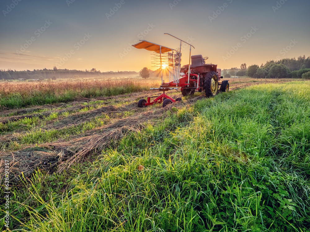Fototapeta premium Old rusty tractor with grass cutting machine in a agriculture field with tall grass at stunning sunrise. Farming industry. Beautiful nature scene at special time. Nobody.