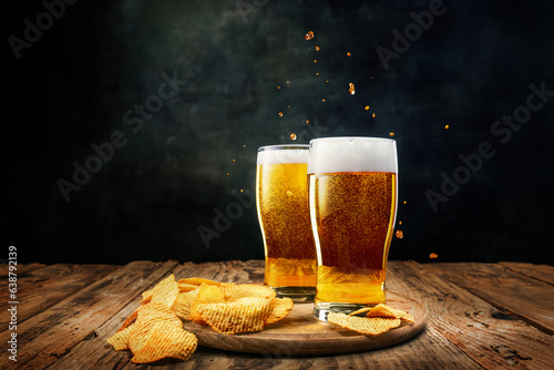 Valokuva Two glasses of foamy, chill, lager beer with chips appetizers on wooden table against dark background