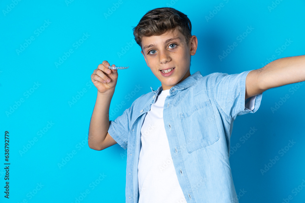 Beautiful kid boy wearing casual clothes make selfie holding an invisible braces aligner, recommending this new treatment. Dental healthcare concept. Beautiful kid boy wearing casual clothes make selfie holding an invisible braces aligner, recommending this new treatment. Dental healthcare concept.