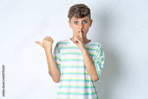 Bilde på lerret Beautiful kid boy wearing striped casual t-shirt asking to be quiet with finger on lips pointing with hand to the side