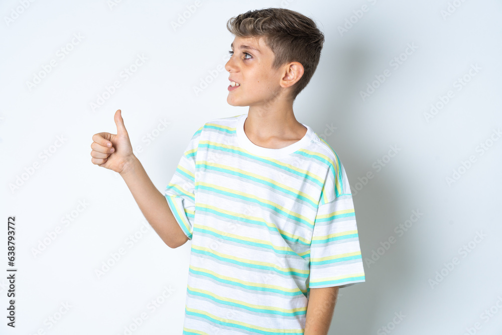 Beautiful kid boy wearing striped casual t-shirt Looking proud, smiling doing thumbs up gesture to the side. Good job! Beautiful kid boy wearing striped casual t-shirt Looking proud, smiling doing thumbs up gesture to the side. Good job!