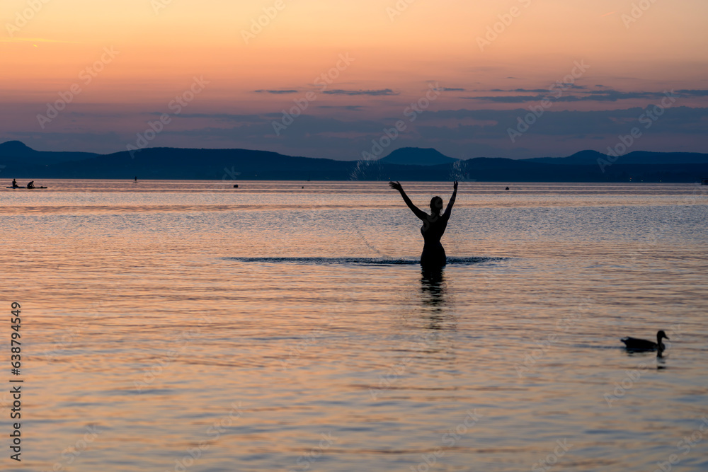 sunset at Lake Balaton with silhouette of night bathing woman and the north part mountains in the background