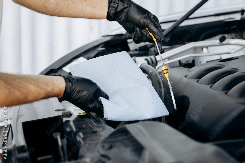 Obraz premium Oil dipstick on the background of a paper towel and a car hood. Engine oil change. Auto mechanic checks the oil level in a car. Work in a car repair shop, service, garage.