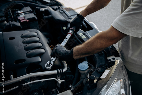 Torque wrench for car repair in the hand of an auto mechanic, wich inspects the hood of the car, carries out repairs or performs maintenance. Working under the hood of a car with tool, without a face