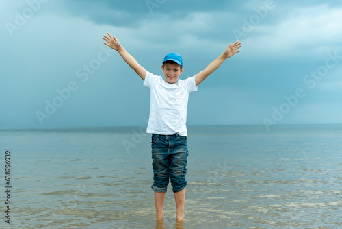 a happy boy stands in the water in the sea and raises his hands up