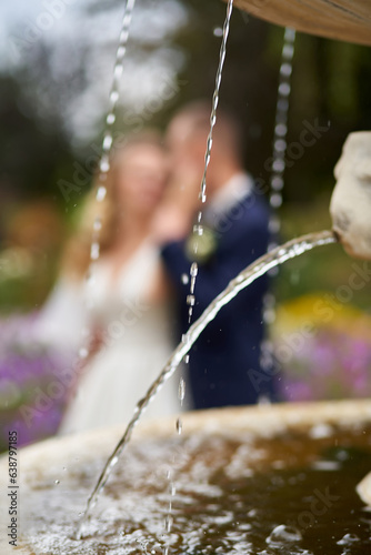 Vertical photo of drops of water flowing from a stone fountain and newlyweds in the background in defocus © Igor