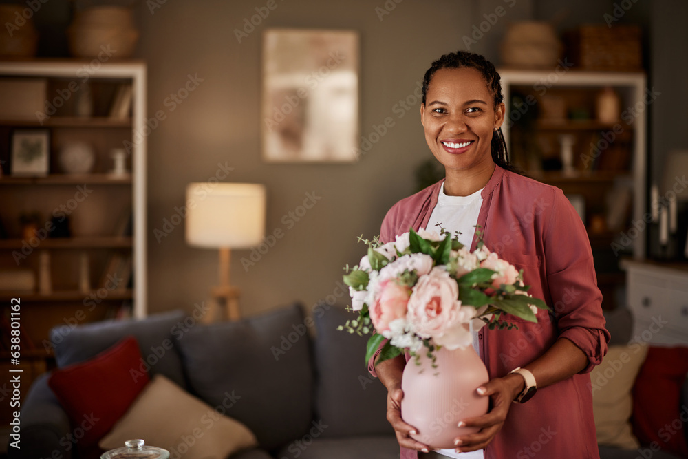 Portrait of an African American woman holding a vase with flowers in the living room.