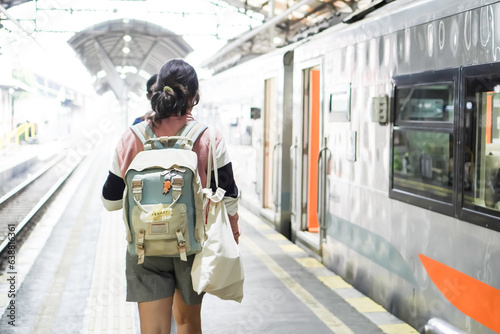 Beautiful happy young asian woman with backpack walking in station platform while looking for her passenger seat in train car. Concept for Solo traveling, vacation, holiday, journey, trip, paid leave.