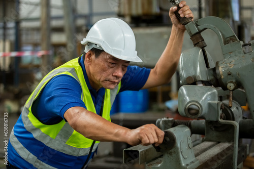 Elderly male worker wear hardhat working at machine in factory. Man technician control metalwork lathe industrial. work factory industrial concept.