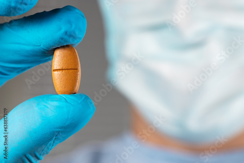 Doctor in mask holding a brown pill with fingers in gloves in the pharmaceutical research laboratory