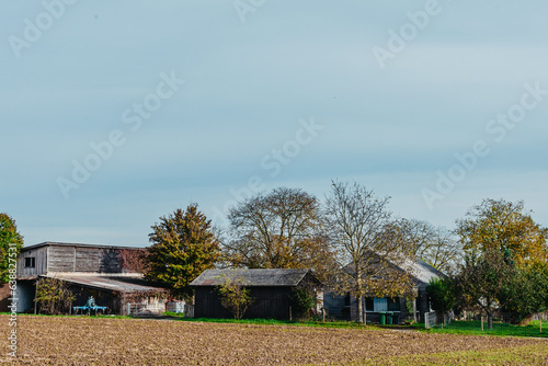 Rural farm in autumn season. Farm in autumn season. Countryside farm house. Farm in autumn scene. Rural scene with houses at the field under cloudy sky in October. Field in first plan.