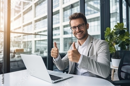 happy businessman in eyeglasses showing thumbs up while working with laptop in office