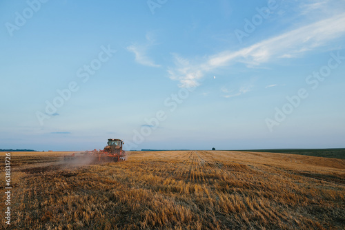 Modern tractor with a heavy trailed disc harrow works a wide hilly field. Autumn or spring agricultural campaign