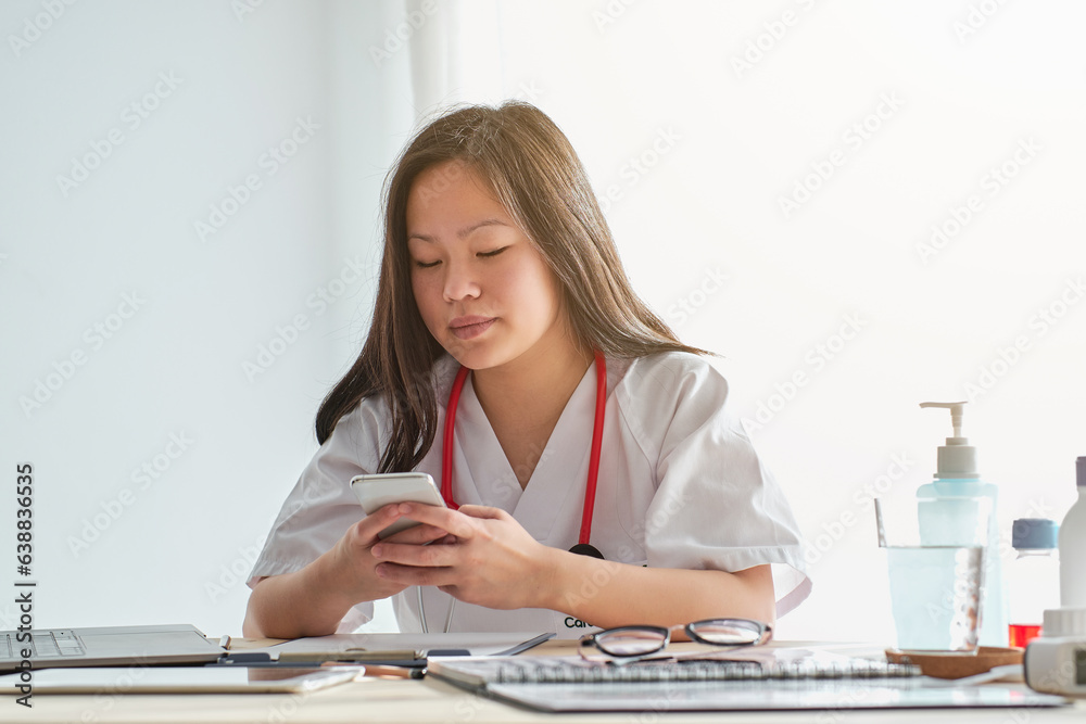 Focused Asian doctor browsing smartphone in hospital Focused Asian doctor browsing smartphone in hospital