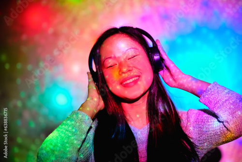 Delighted Asian woman listening to music in studio with glowing