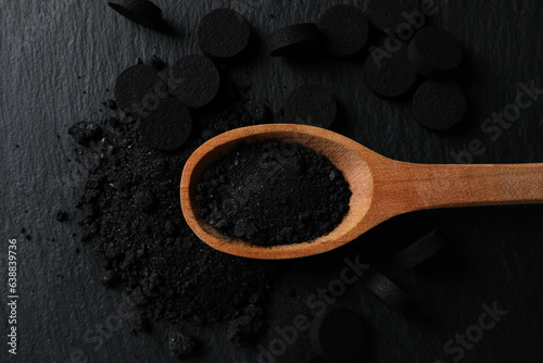 Activated charcoal powder in a wooden spoon on a dark background