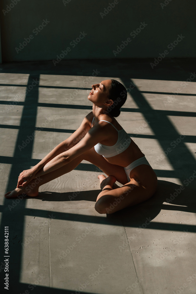 Dark room with sunlight. Young woman with slim body type is in fitness clothes in the studio