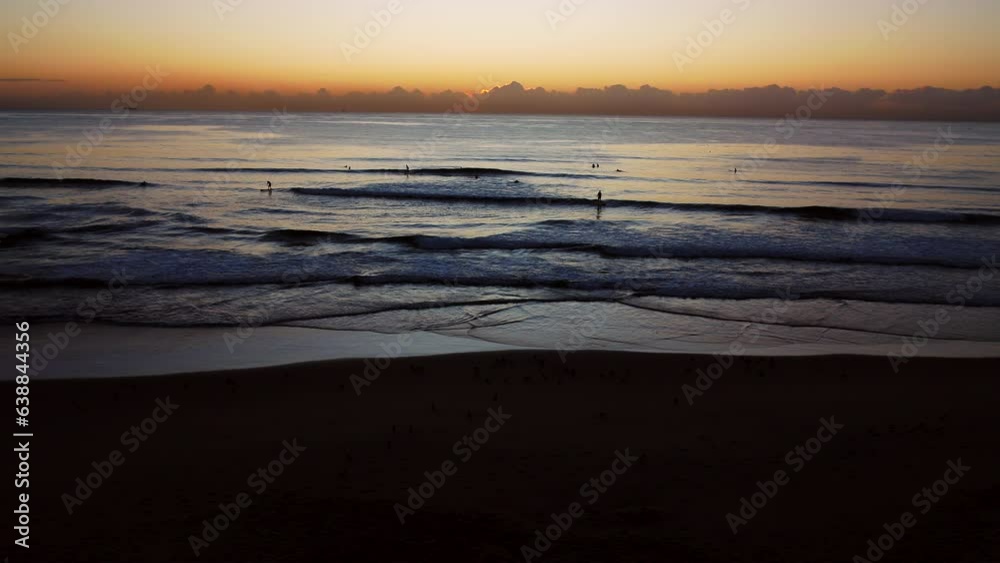 In the early morning, the sun rises behind clouds on the horizon as surfers ride the calm sea in Durban, with pigeons flying past in the foreground. In the early morning, the sun rises behind clouds on the horizon as surfers ride the calm sea in Durban, with pigeons flying past in the foreground.
