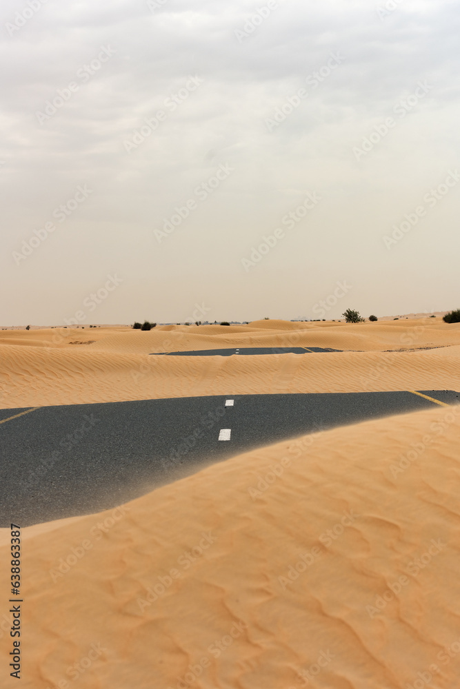 (Selective focus) Stunning view of a deserted road covered by sand dunes. Empty road that run through the Dubai desert. Dubai, United Arab Emirates, (UEA)